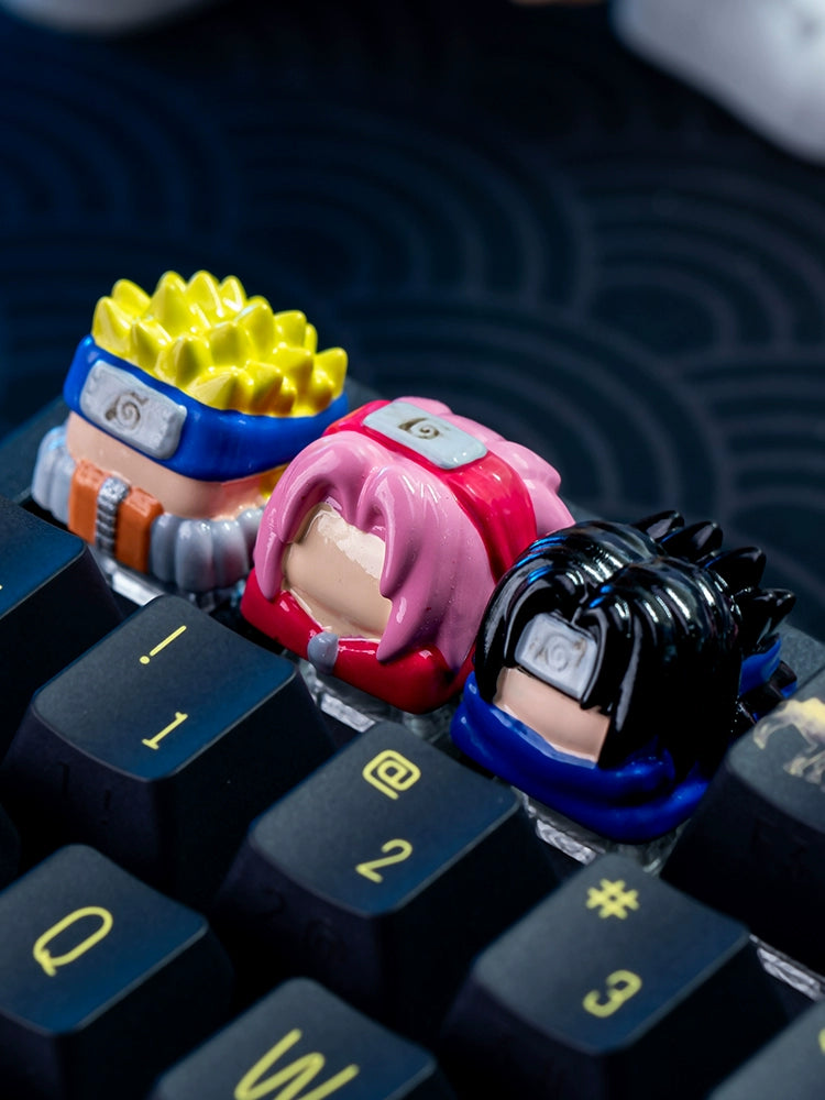 The Team 7 Naruto Keycap Set by Naruto features three custom resin keycaps, each representing the anime characters Naruto, Sakura, and Sasuke with distinct designs. The keycaps display unique hairstyles and headbands in yellow, pink, and black on a mechanical keyboard.