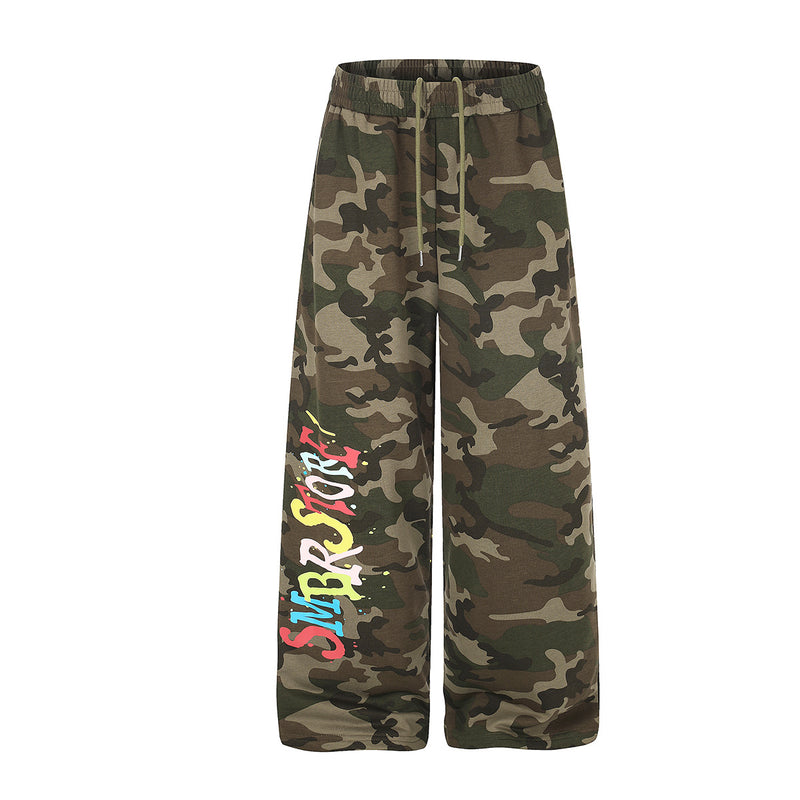 Weite Camouflage-Sweathose mit mehrfarbigem Graffiti-Schriftzug am linken Bein und Farbspritzern, Vorder- und Rückansicht