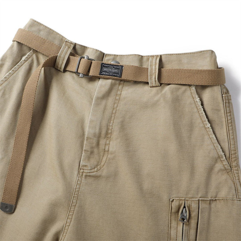 Close-up of khaki cargo shorts waistband with woven belt and zip pocket edge