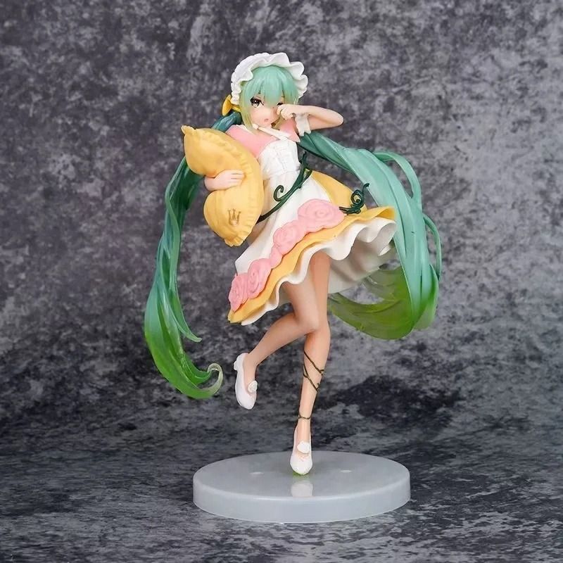 The Hatsune Miku Sleeping Beauty PVC Figure depicts a female anime character with long green hair, wearing a frilly white and pink dress and white shoes. She holds a yellow pillow, and her hair and clothing feature detailed flowing designs. The figurine stands on a simple round white base.