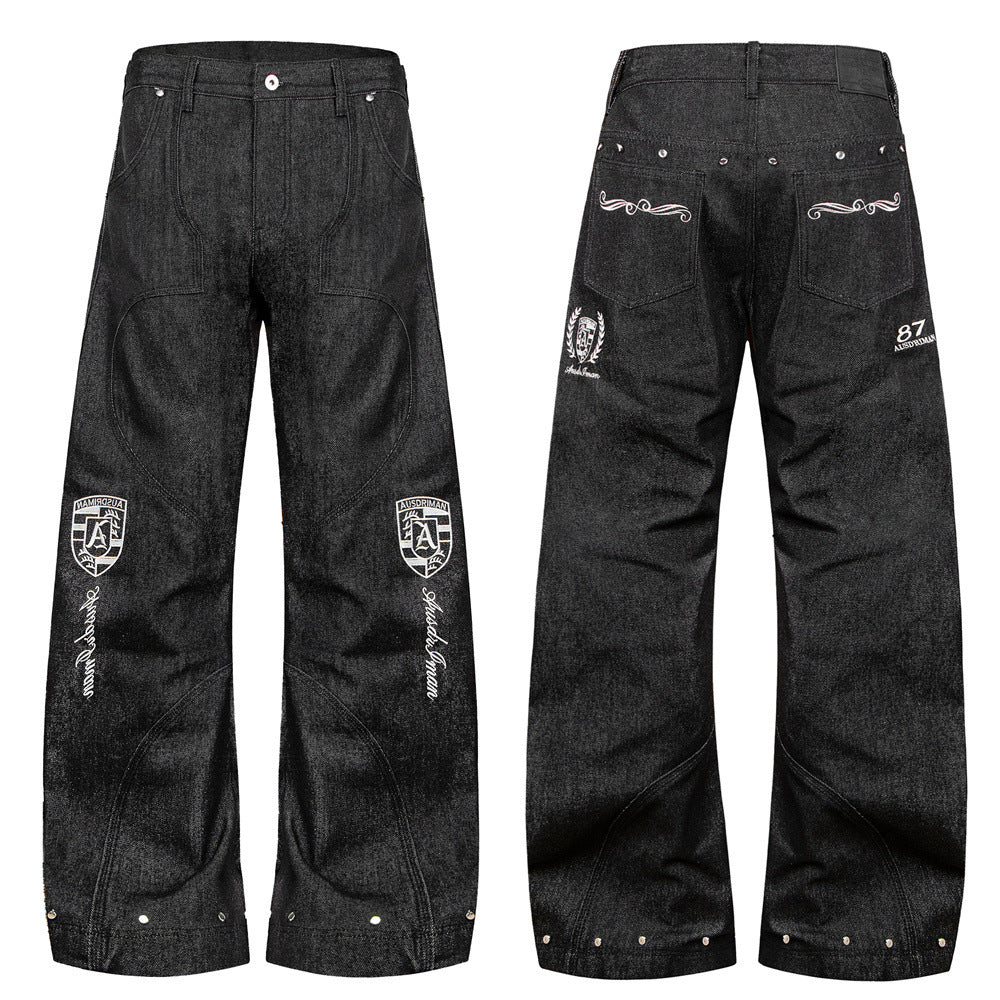 Jean homme noir à jambes larges, avec motifs brodés d’écussons bouclier, coutures patchwork déconstruites et détails de rivets argentés à l’ourlet