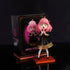 The Spy x Family Anya Forger PVC Figure, featuring a 17 cm pink-haired character with starry eyes, dons a black dress with gold trim and stands on a wooden base. The box showcases artwork of Anya, proudly labeled from "Spy × Family.