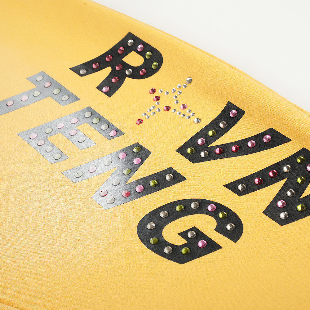 Close-up of rhinestone letter print on yellow sweatpants leg