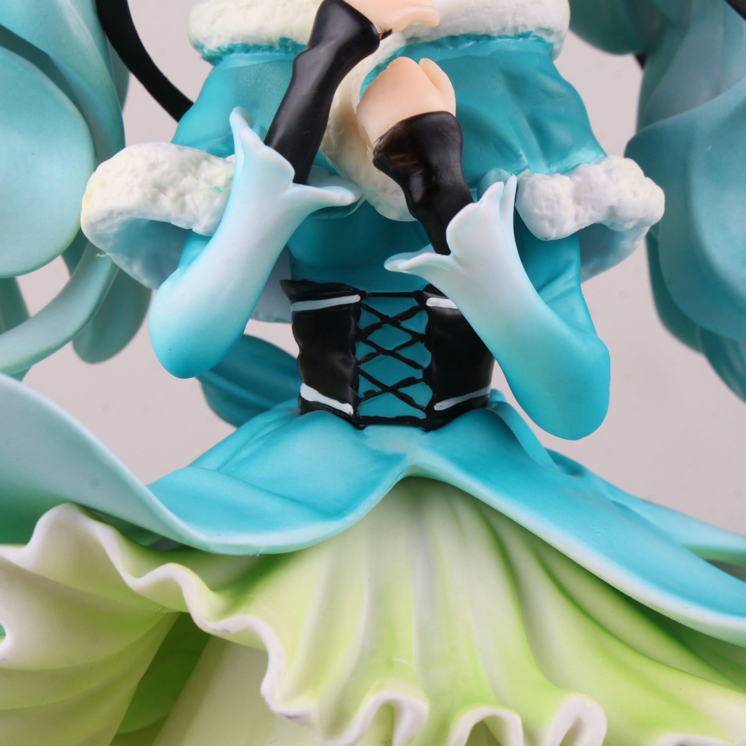 Close-up of a Hatsune Miku 1/7 Scale PVC figure in an elegant pose with flowing hair, featuring a teal and white dress, black corset, lace-up detail, long gloves, a fluffy collar, and layered blue and lime green skirt. Hands are positioned near the face.