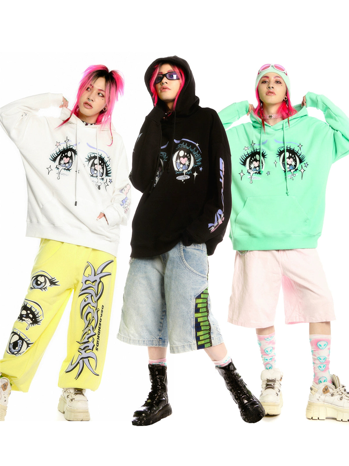 Three pink-haired individuals wear oversized Seakoff Kawaii Aesthetic Crying Eyes Hoodies in white, black, and mint green, each with large eye designs. They pair them with baggy shorts, sunglasses, and chunky footwear against a pristine white backdrop.