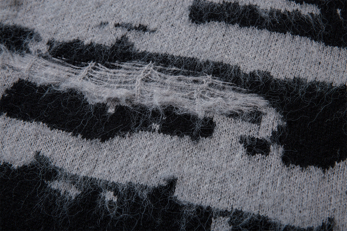 Close-up of a horizontal distressed knit section with loose gray fibers across the black and gray pattern
