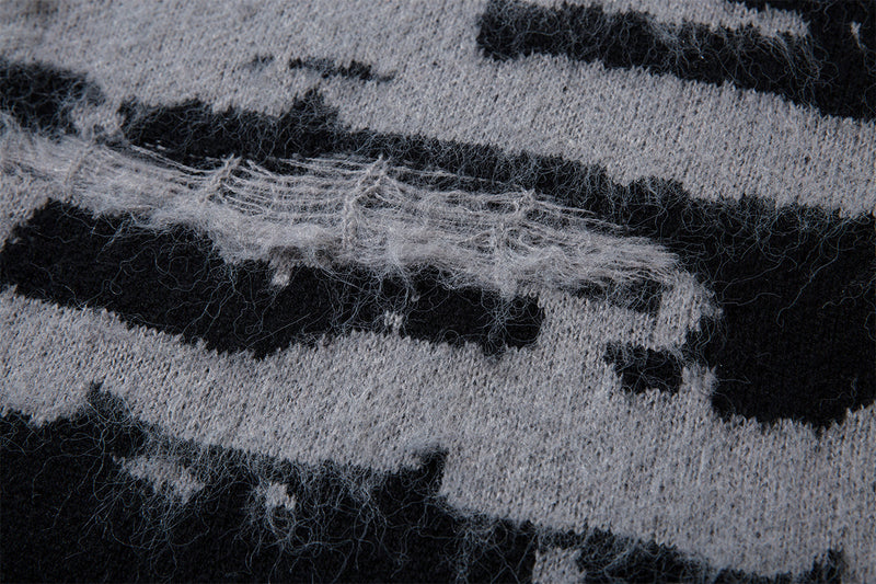 Close-up of a horizontal distressed knit section with loose gray fibers across the black and gray pattern