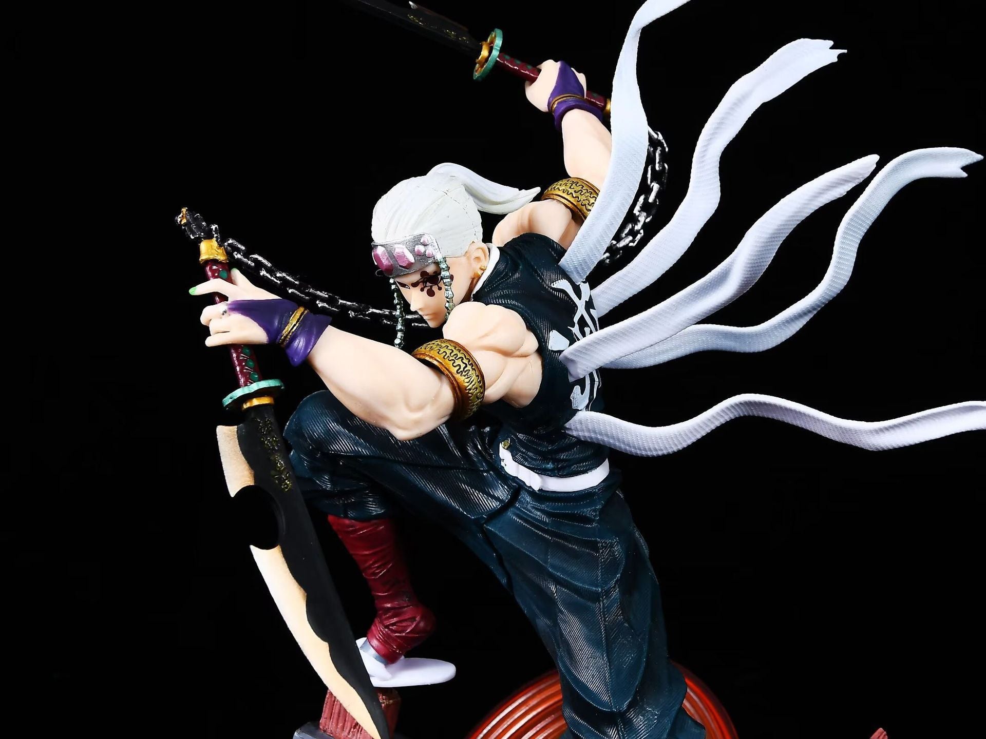 The Tengen Uzui Battle Sound Pillar Figure from Demon Slayer, crafted in high-quality PVC, features the Sound Hashira with long white hair, dual swords, and dynamic ribbons. Wearing a dark sleeveless outfit and red boots, the 27cm GK model poses on one knee against a black background.