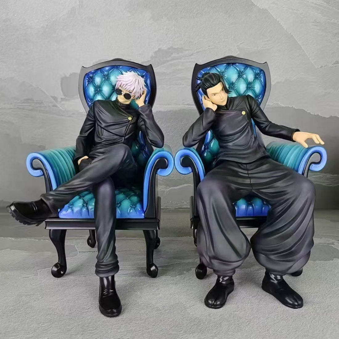 The Jujutsu Kaisen Satoru Gojo &amp; Suguru Geto Sitting Posture PVC Figure Set features two figures on ornate blue chairs: Satoru with white hair and sunglasses, and Suguru with black hair. Both wear black outfits and sit relaxed, one hand near their face.