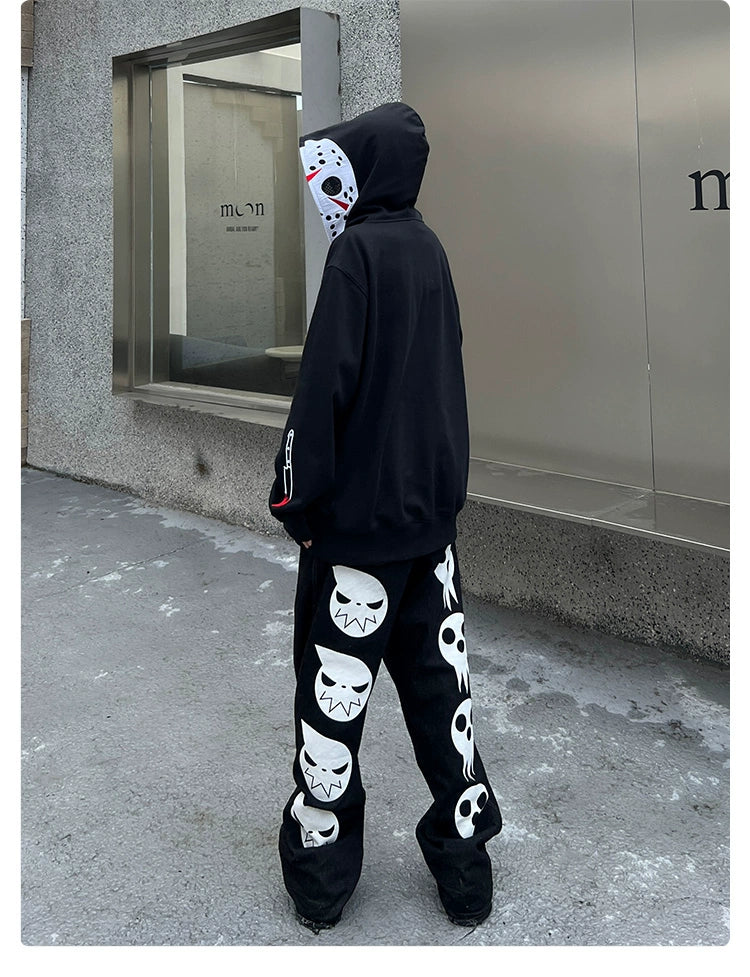 Someone in a Seakoff Friday the 13th 400GSM Oversized Jason Mask Zip-Up Sweatshirt stands facing a concrete building with large glass windows. They&