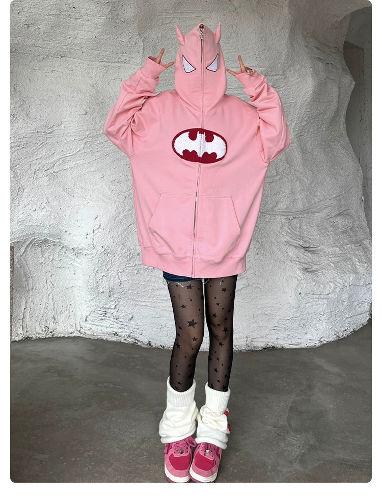 Someone is wearing a Seakoff Batman-Inspired Hoodie - a 400GSM oversized pink zip-up superhero sweatshirt. They pair it with black star-patterned tights, leg warmers, and pink sneakers, posing playfully with raised hands.