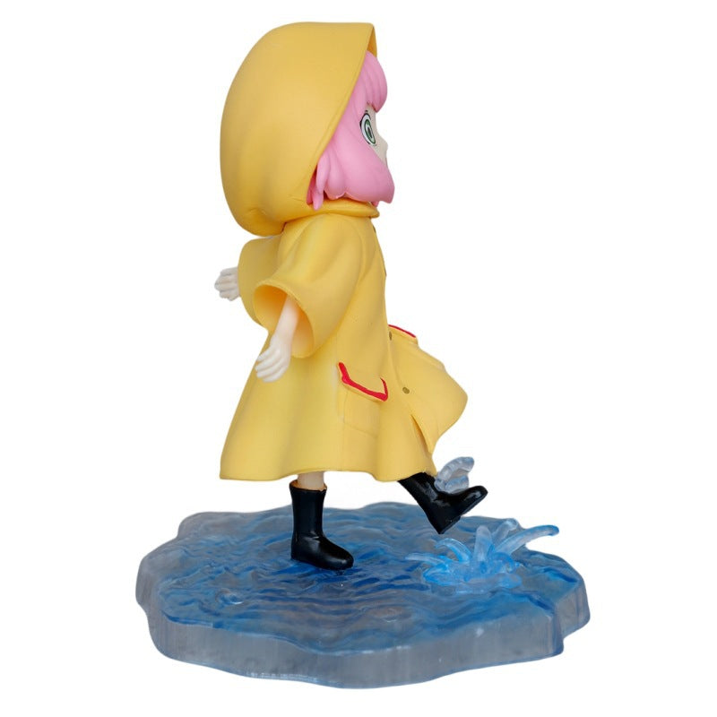 The Anya Forger Yellow Raincoat Figure, a cute PVC anime collectible from the Spy × Family brand, features a child in a yellow raincoat with black boots and pink hair stepping on a puddle. Set on a water-like textured base, the hood is down.