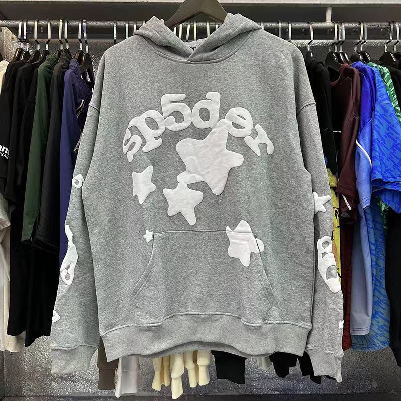 The Classic Grey Sp5der Hoodie by Sp5der stands out in streetwear fashion with its trendy star print and bubble-style &quot;sp5der&quot; text. Featuring a front pocket and drawstring hood, it&