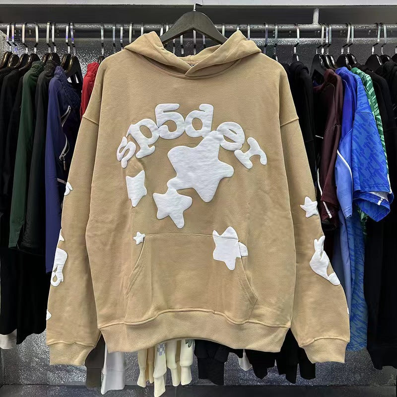 A Chic Brown Sp5der Hoodie by Sp5der, featuring trendy star print and white star/cloud appliqués, hangs on display among other vibrant streetwear. This cozy sweatshirt is a stylish wardrobe staple.