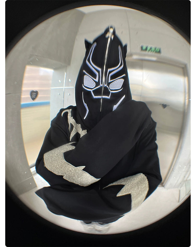 A person indoors wears a Seakoff Black Panther-Inspired Hoodie, an oversized 400GSM superhero zip-up sweatshirt with ear design. The popular streetwear piece features white stylized patterns and is paired with a black mask, while the fisheye lens distorts the surroundings.