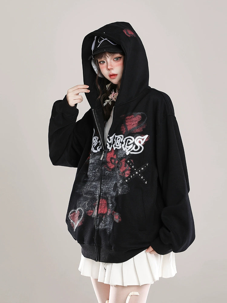 A person sports an oversized black Seakoff Gothic Hello Kitty Princess Hoodie with edgy heart and cross graphics. They wear the hood up, paired with a cap and white skirt, creating an alternative fashion vibe against a plain, light background.