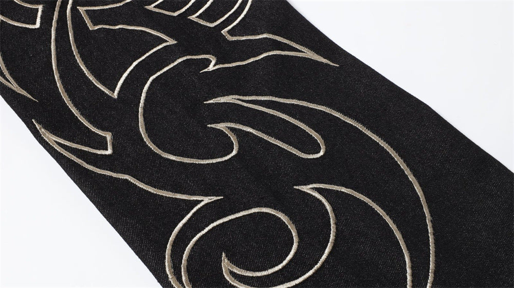 Close-up of black denim leg with pale embroidered flame design