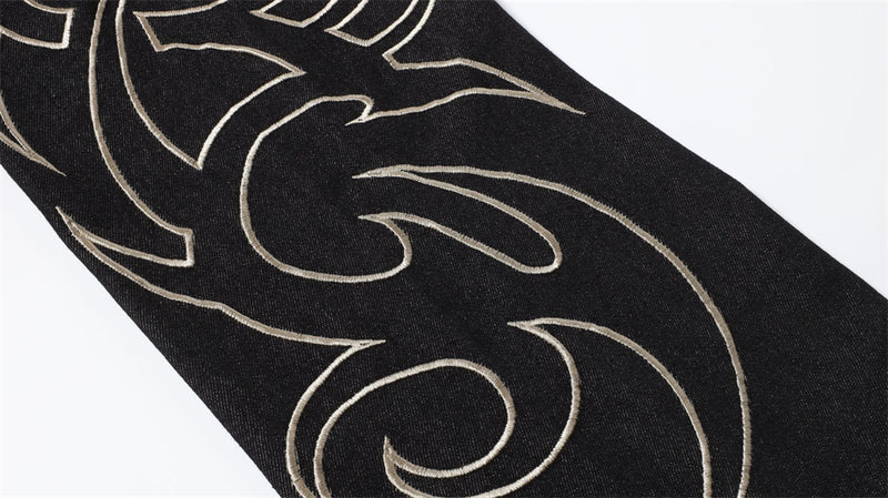 Close-up of black denim leg with pale embroidered flame design