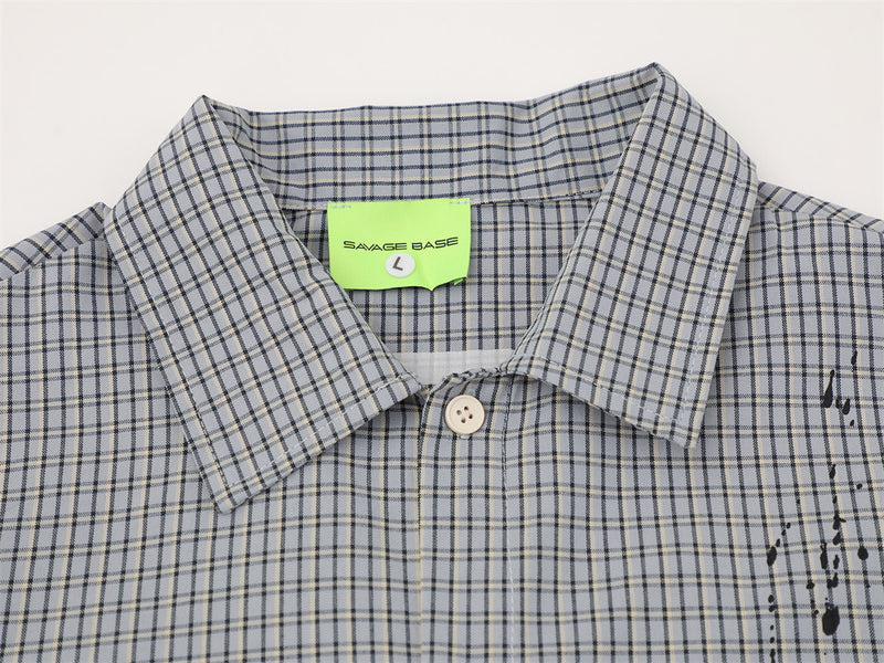Close-up of shirt collar and top button on gray plaid fabric with black paint splatter