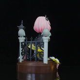 The Spy x Family Anya Forger PVC Figure – 19 cm showcases a charming collectible with pink hair on a brown base, surrounded by a black fence and gray posts, complete with a small lantern and white and yellow flower.