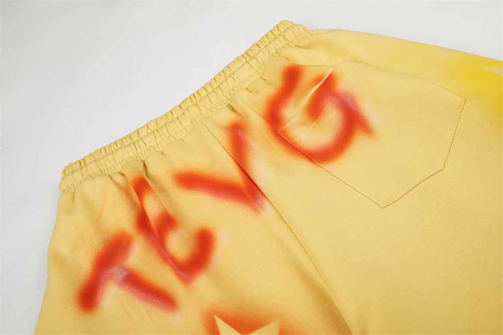Close-up of yellow sweatpants back pocket and waistband with orange spray-dye lettering