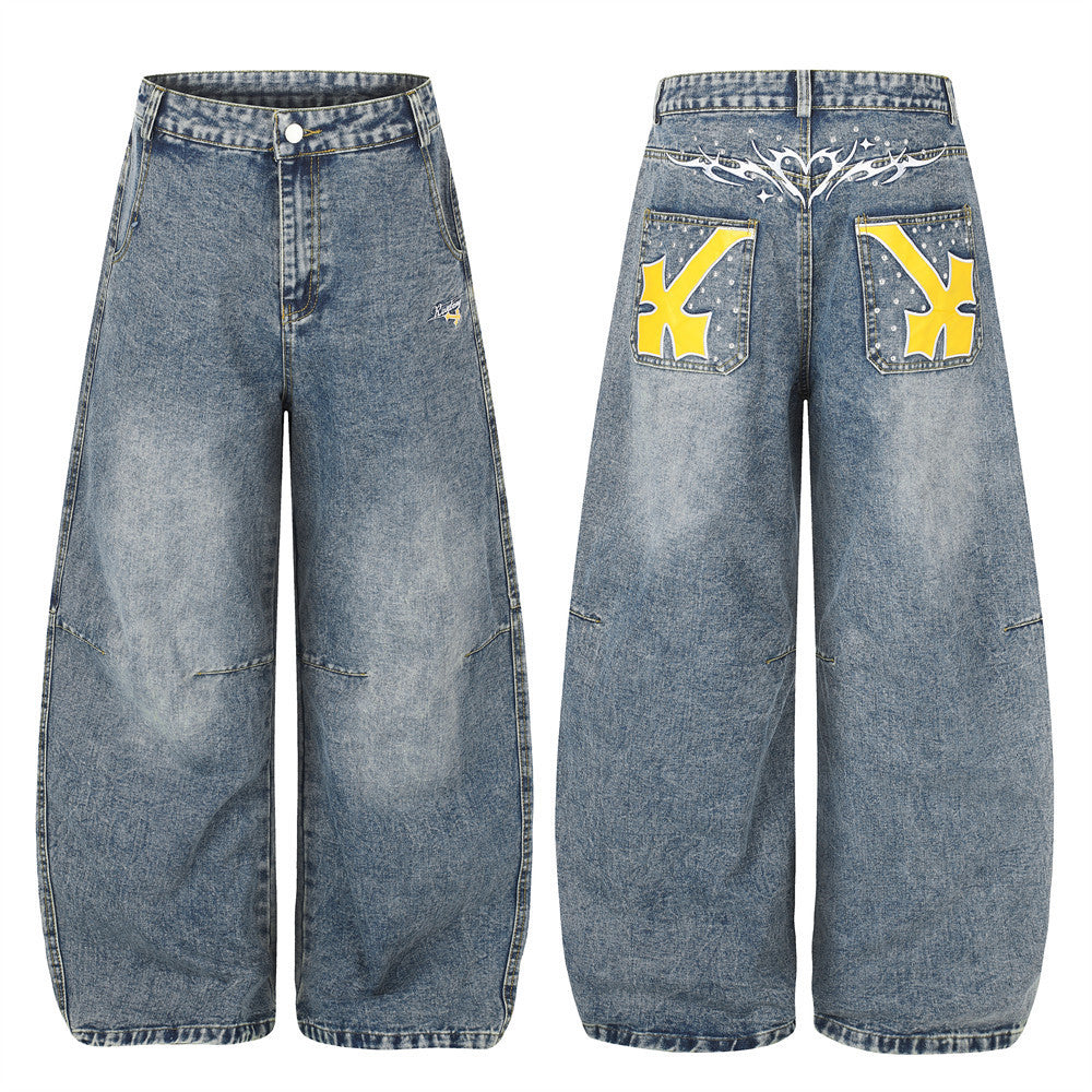 Wide-leg baggy jeans in washed blue denim with yellow cross embroidery on back pockets and tribal graphic yoke detail