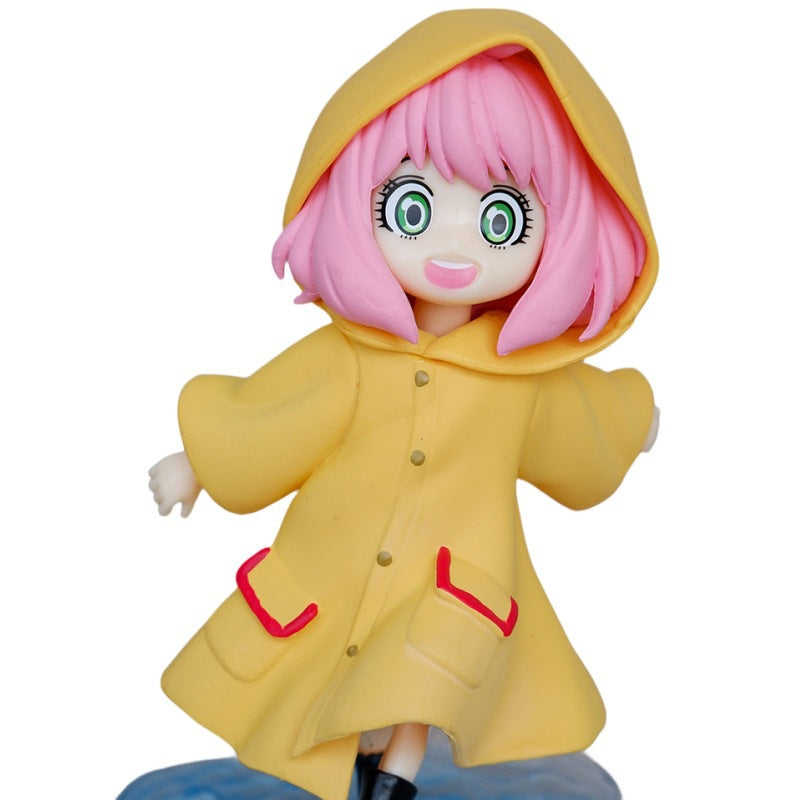 The Anya Forger Yellow Raincoat Figure - Cute PVC Anime Collectible by Spy × Family captures the charm of the collection with pink hair, large green eyes, and a warm smile in her yellow hooded coat with red-trimmed pockets, all on a blue base.