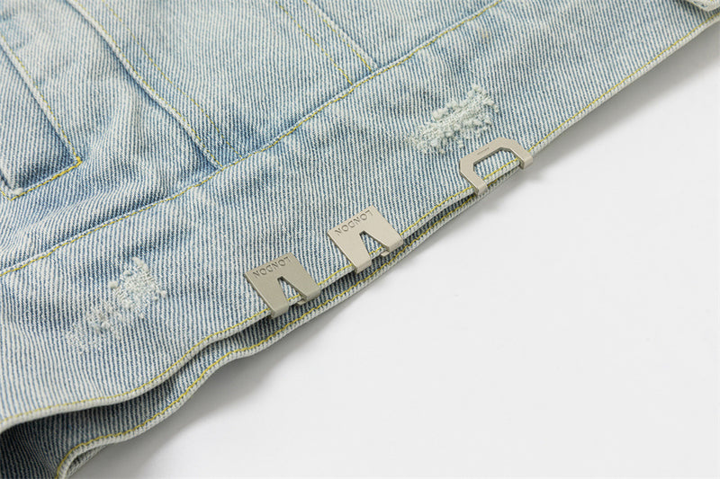 Close-up of the jacket hem with silver-tone metal tabs and multiple frayed distressed patches