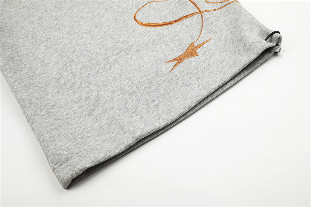 Close-up of gray sweatpants hem with brown script embroidery and star detail