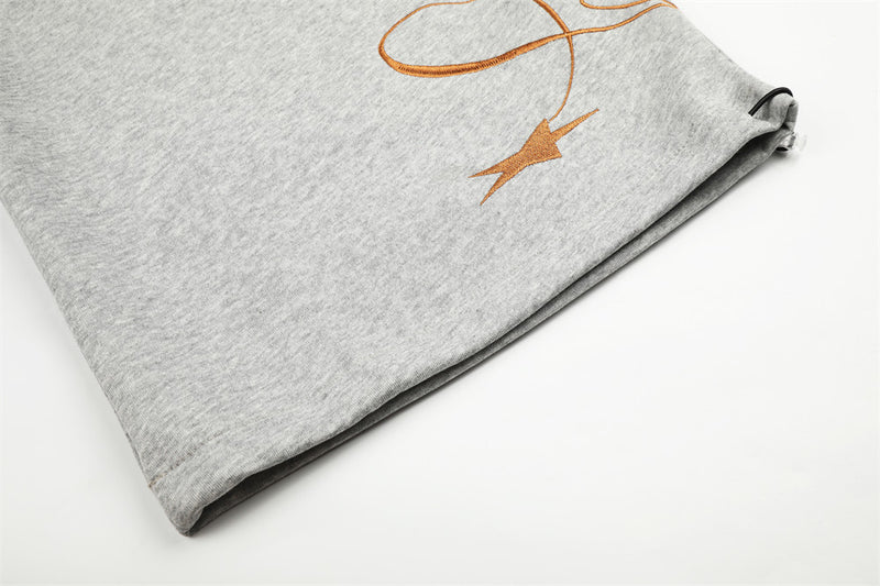 Close-up of gray sweatpants hem with brown script embroidery and star detail