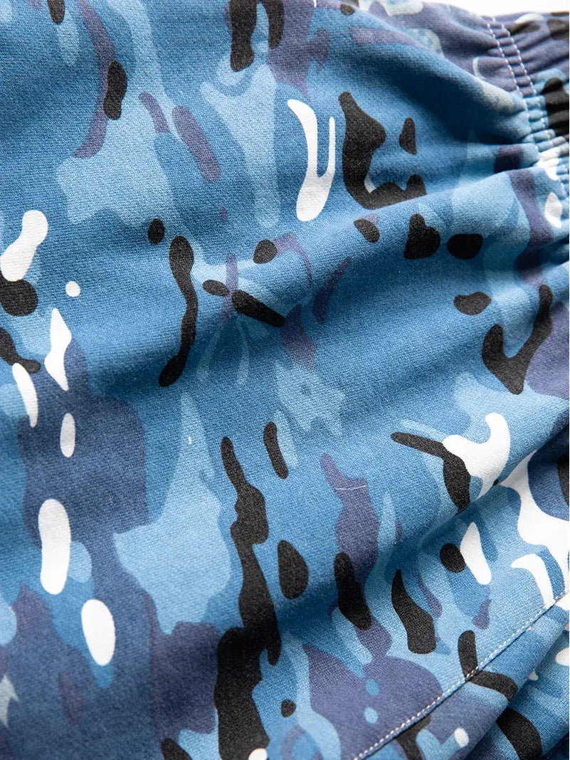 Close-up of Men's Blue Camo Drawstring Shorts—relaxed fit cotton with abstract black, white, and light blue camouflage. The slightly wrinkled fabric and elastic waistband highlight these stylish streetwear shorts.