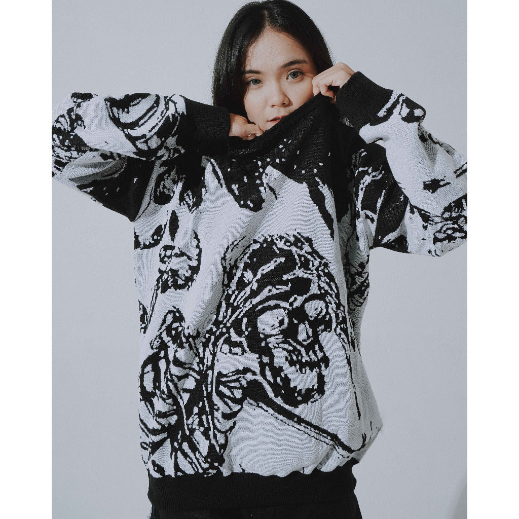 A person with long dark hair wears the Seakoff Premium Skeleton Warrior Knit Sweater, showcasing bold gothic fashion. They partially cover their face with the black and white jacquard design sweater while standing against a plain background.