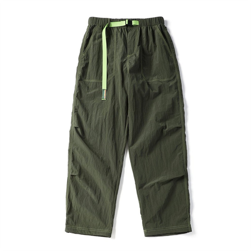 Front view of olive green parachute pants with a bright green drawcord, belt, and cargo pockets