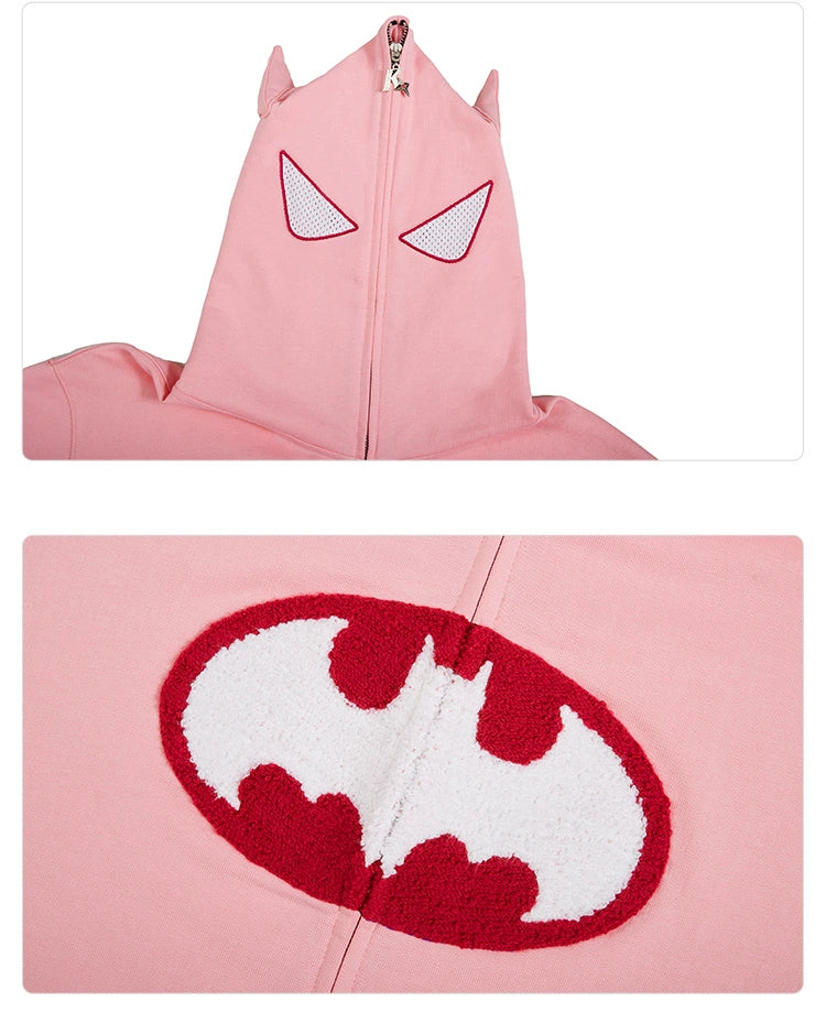 The image showcases the Seakoff Batman-Inspired Hoodie, a pink oversized zip-up sweatshirt with pointed bat-like ears and mesh eye cutouts on the hood. A red and white bat emblem embellishes the fabric, ideal for superhero enthusiasts.