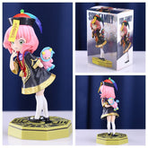 The Spy × Family Anya Forger PVC Figure stands 18 cm tall, showcasing Anya in a school uniform with pink hair and a black-and-gold outfit on a decorated hexagonal base while holding a small blue plush toy. The box behind has identical character branding, and multiple angles are displayed.