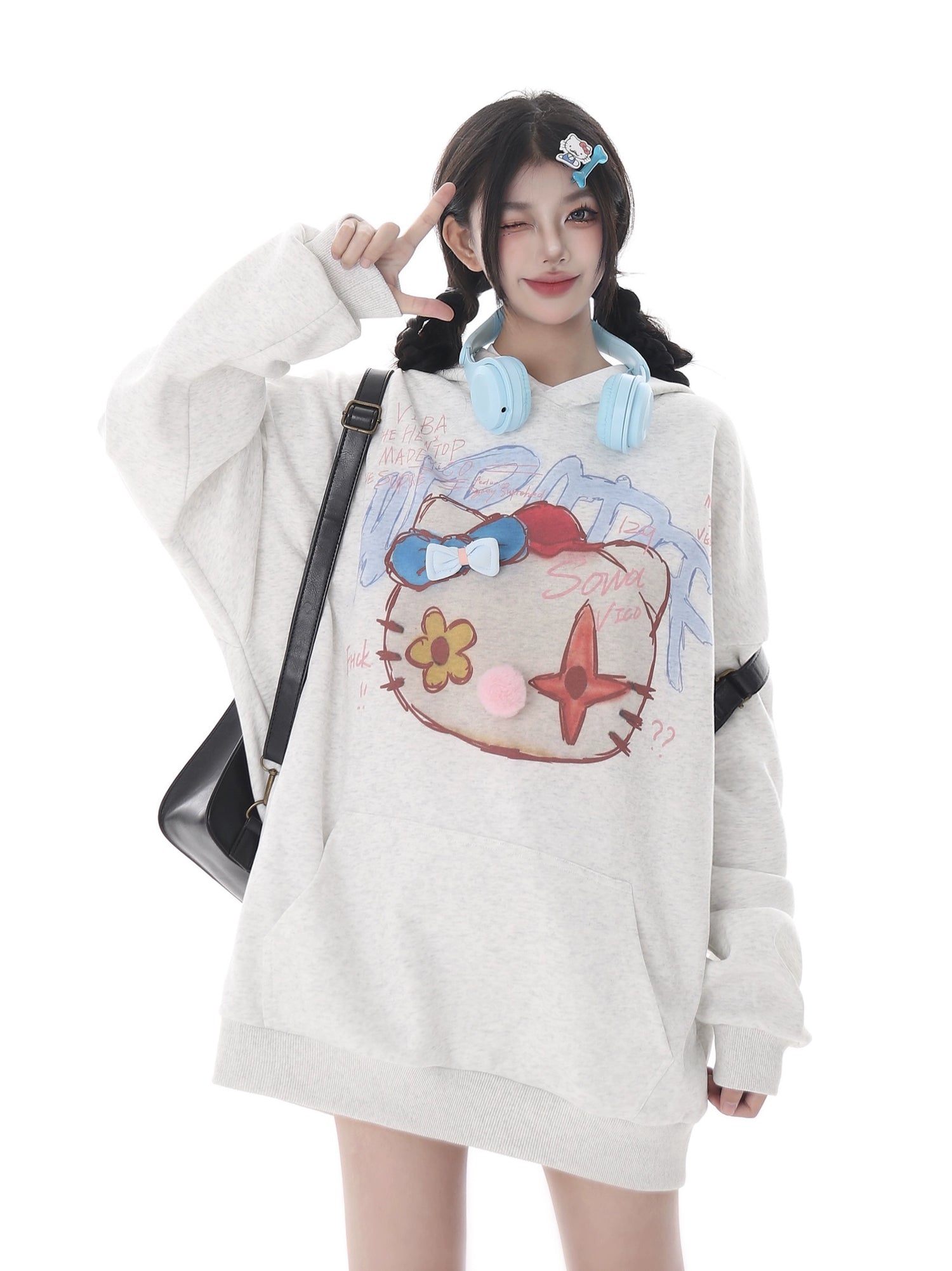 A person with long dark hair, wearing a Seakoff Kawaii Pom-Pom Crown Hoodie in white featuring colorful graphics, and blue headphones around their neck. They carry a black shoulder bag, exuding a kawaii streetwear vibe against a plain white background.