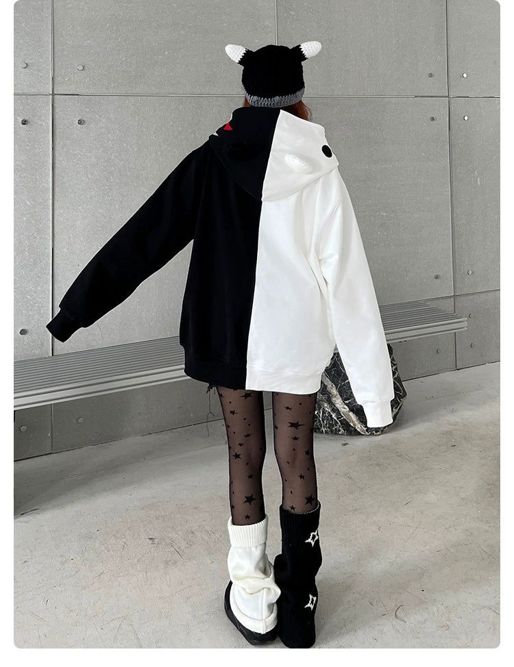 Facing away from the camera, a person wears a Seakoff Monokuma-Inspired Hoodie, an oversized black and white Danganronpa zip-up sweatshirt. They also don a black beanie with white horns, patterned tights, and boots with leg warmers in an indoor setting featuring a metallic wall and bench.