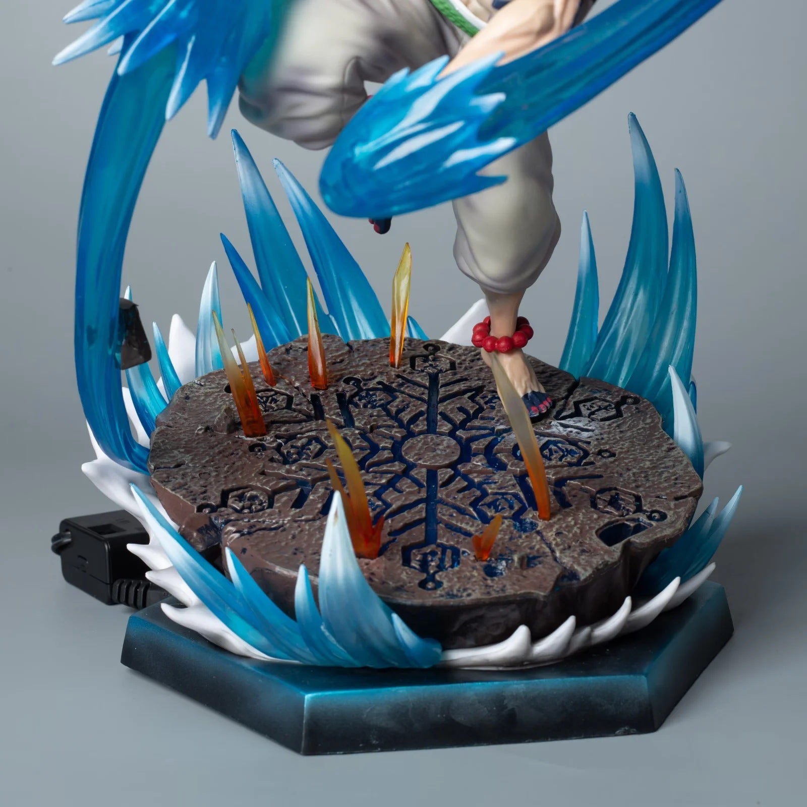 The Rengoku Kyojuro Demon Slayer Figure is a 26cm PVC anime collectible with dynamic ice powers. It features a detailed base with blue symbols, wave-like spikes, orange flames, and a sword-wielding hand reminiscent of the Flame Hashira design. An attached wire is visible for light-up effects.