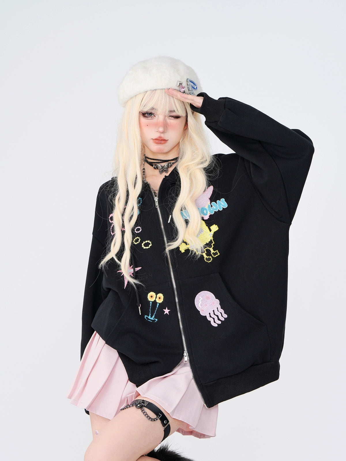 A person with long blonde hair poses against a plain background, wearing a Seakoff Kelly Kitty Pastel Kawaii Hoodie featuring adorable embroidered characters, complemented by a white beret, light pink skirt, and choker necklace. They effortlessly capture the essence of Japanese Streetwear.