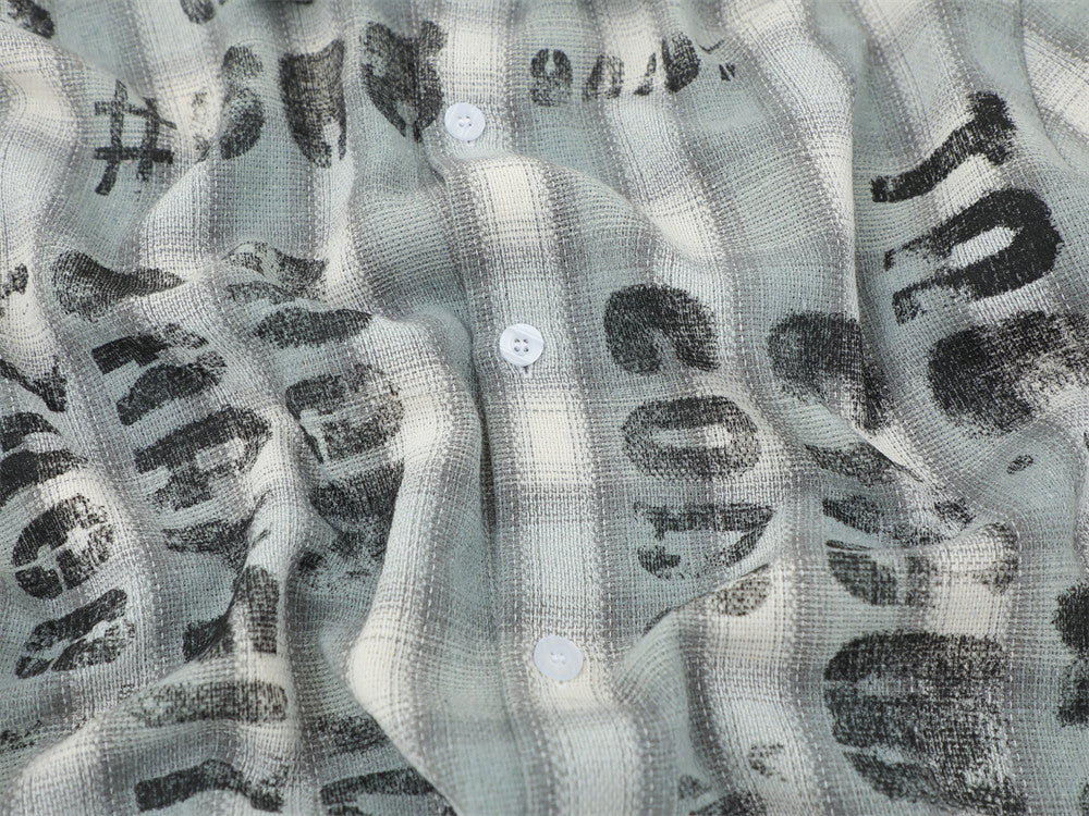 Close-up of the front placket on a light gray plaid shirt with distressed black lettering