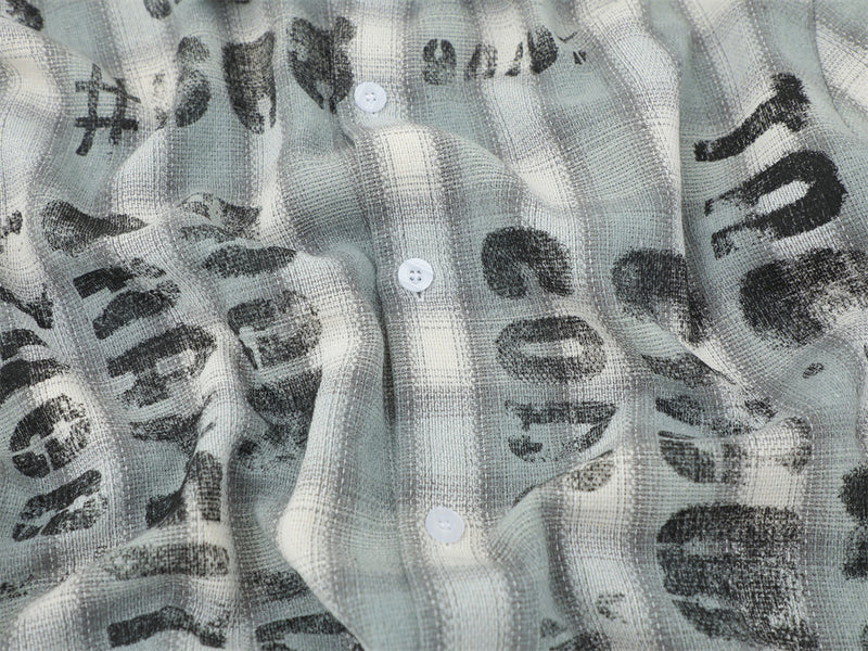 Close-up of the front placket on a light gray plaid shirt with distressed black lettering