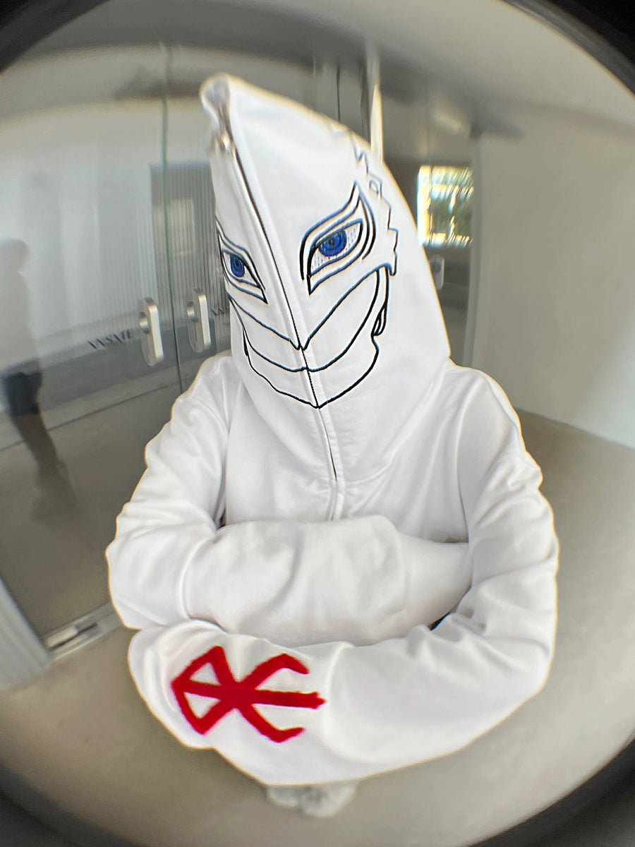 Wearing the Berserk Griffith-Inspired Hoodie, a white oversized zip-up anime sweatshirt, this person showcases a graphic of eyes and stylized face on the hood. The red symbols on one sleeve are inspired by Berserk&