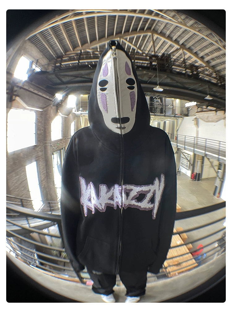 In an industrial-style building with metal railings and large windows, someone in a No-Face Anime Hoodie—part of the Spirited Away collection—and a white mask adorned with black and purple details makes a striking impression.