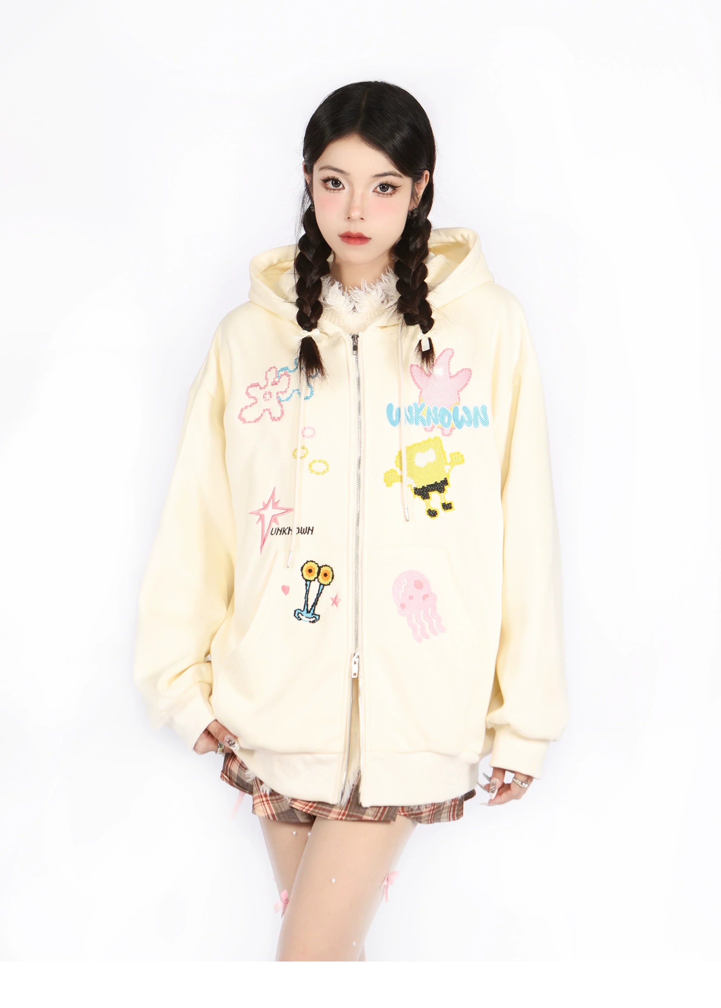 Wearing a Kawaii Pastel Cartoon Hoodie by Seakoff, featuring playful embroidered designs like a jellyfish and robot, a person with braided hair poses seriously in plaid skirt and stockings on a white backdrop.