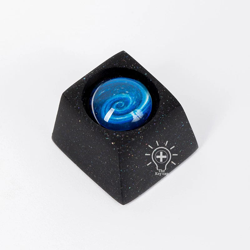 A black high-quality resin keycap from the &quot;Naruto Elements Keycap Set&quot; features a glossy blue galaxy swirl, with &quot;The Keycap&quot; printed in white at the base.