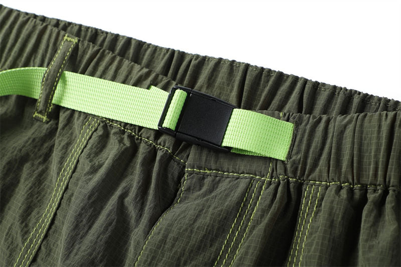 Close-up of the olive pants waistband showing a bright green clip belt and elastic gathering