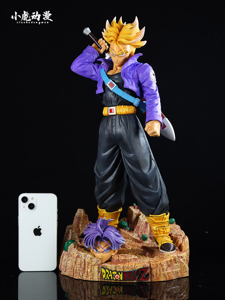 The Seakoff Trunks Collectible Figure from Dragon Ball Z showcases a spiky yellow-haired character in a purple jacket, sword over his shoulder. Standing on a rocky base, it includes an extra head and smartphone for scale, with &quot;Dragon Ball Z&quot; inscribed on the base.