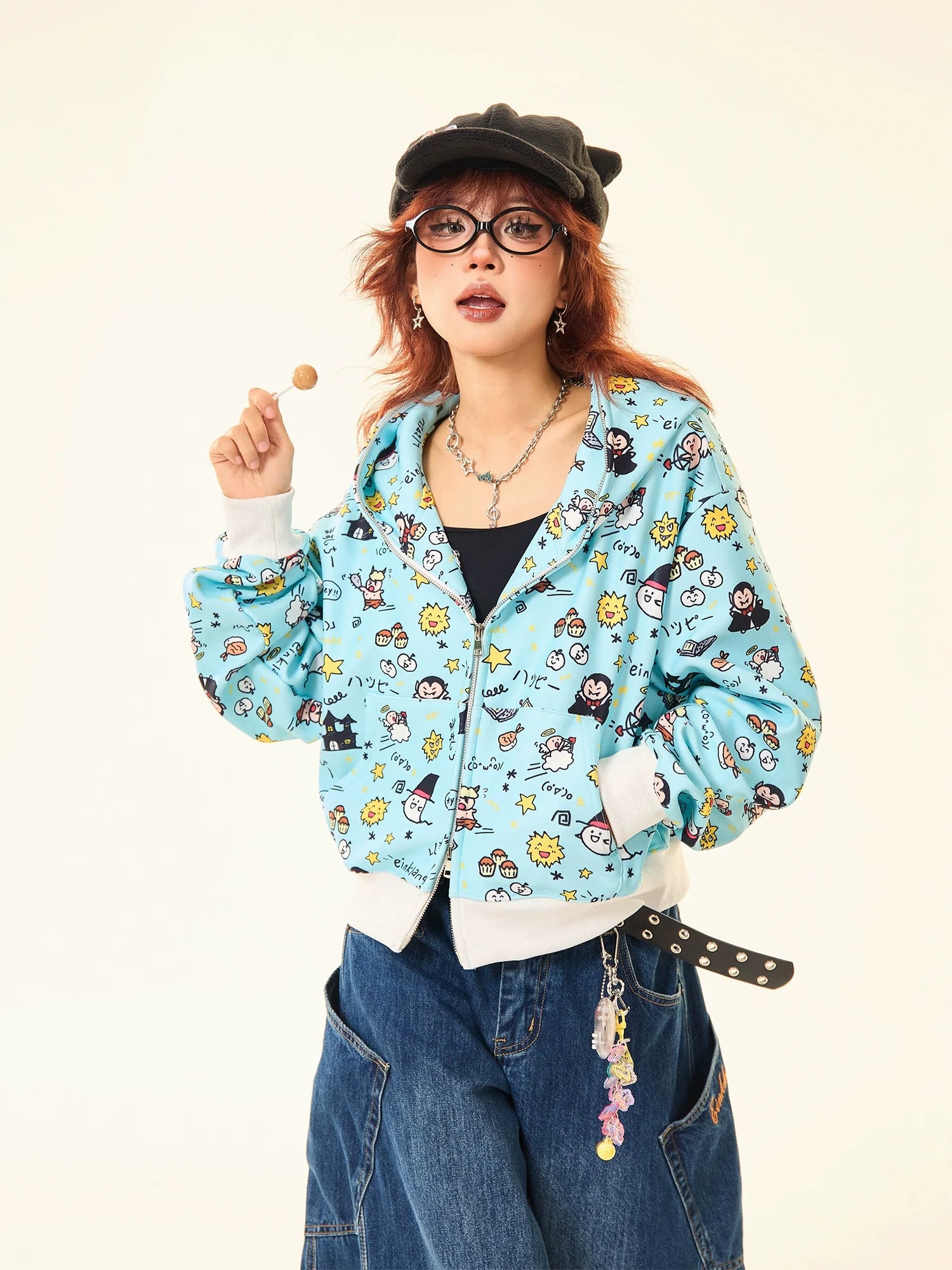 A red-haired person sports a black cap, round glasses, wide-leg jeans, and a whimsical streetwear look featuring Seakoff's Kawaii Cartoon Bear Hoodie with adorable ears. Playful accessories dangle from their belt while they hold a lollipop in one hand.