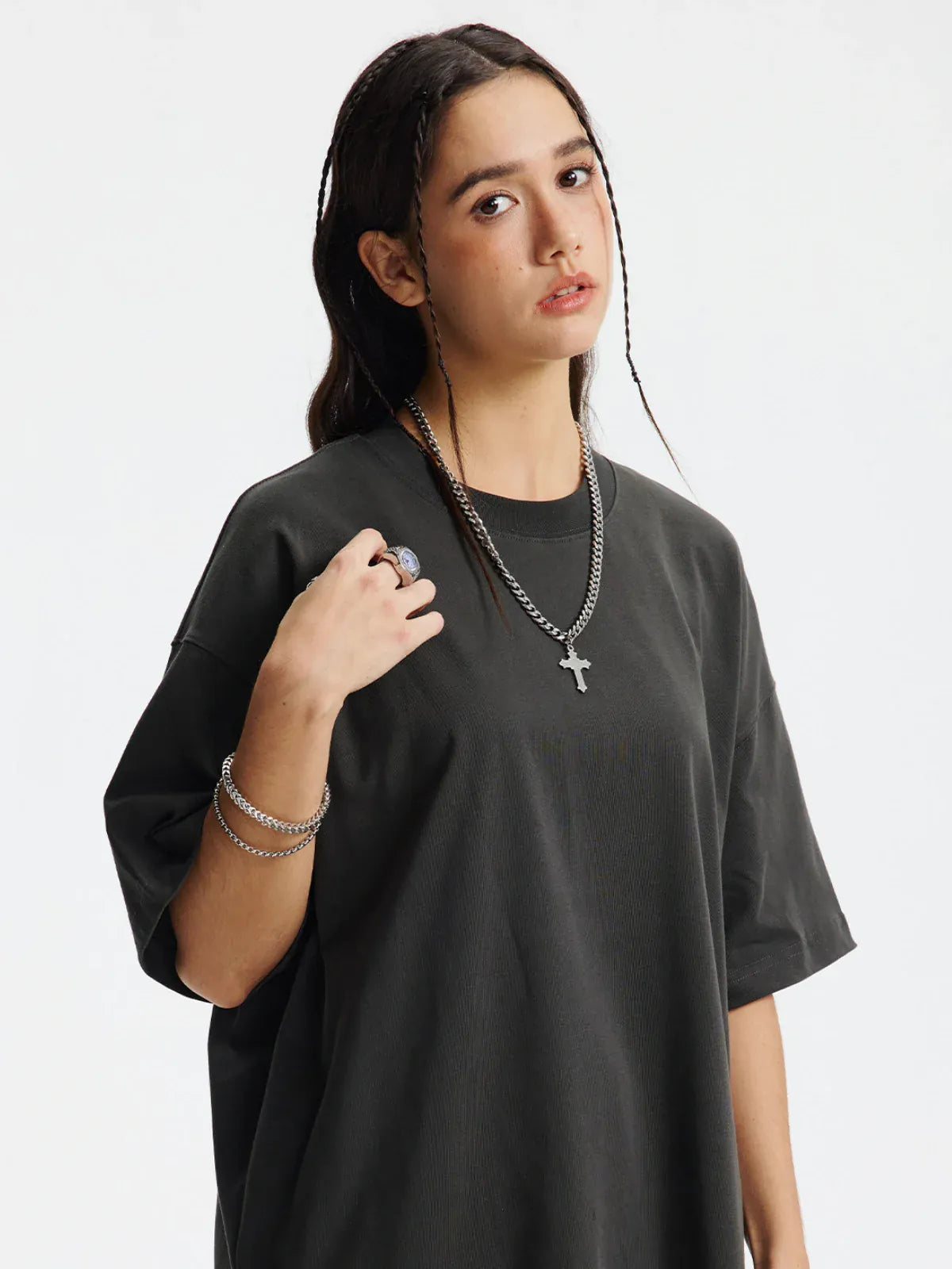 A young woman with long braided dark hair wears a Custom Anime Character Charcoal T-Shirt (230GSM 100% cotton), paired with silver chains, rings, and bracelets, standing against a plain white background.