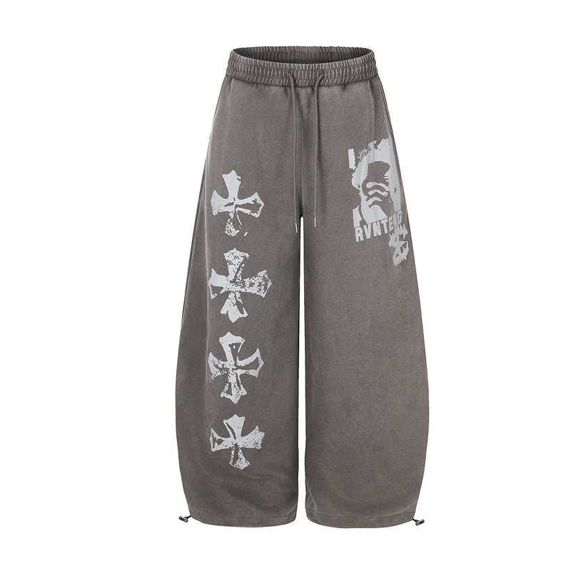 Pantalón de chándal de pierna ancha con efecto lavado ácido, estampado de cruz desgastada en la pierna izquierda y estampado de rostro en el muslo derecho, mostrado en lavado